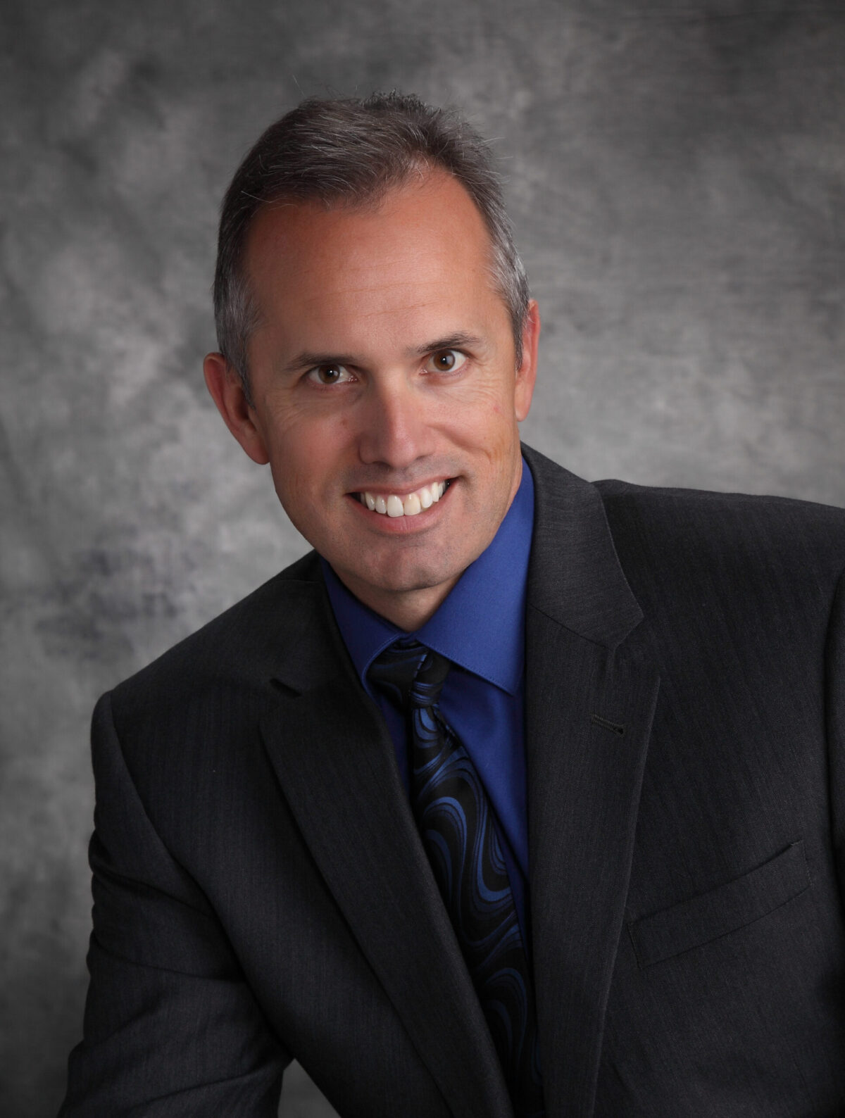 Professional man in a suit smiling against a gray backdrop.